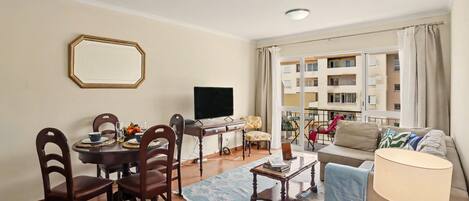 A living room with a dining table, chairs, a TV, a sofa, and a window with curtains.