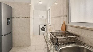Une cuisine compacte dotée d’un évier en acier inoxydable, d’un lave-linge encastré et d’un réfrigérateur.