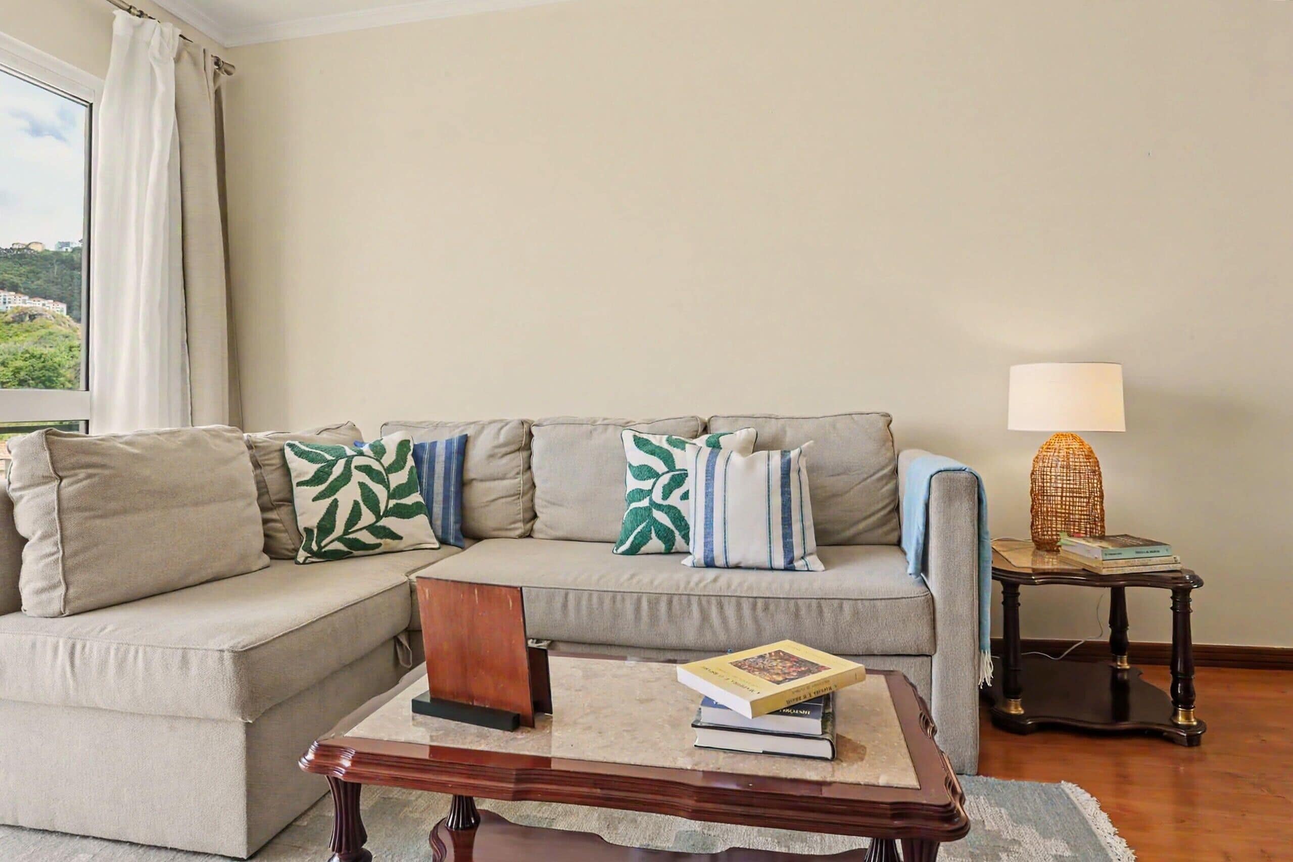 A living room with a sofa, a coffee table, a lamp, and a view of greenery outside.