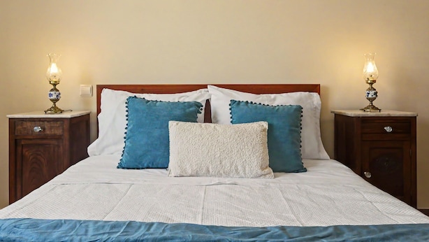 Un lit bien fait, recouvert d’une couvre-lit blanche et bleue, avec deux oreillers assortis et deux tables de chevet dotées de lampes.