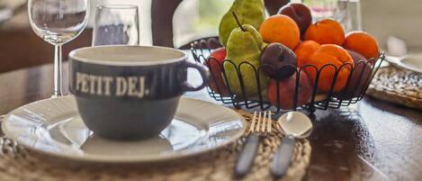 A dining table with a bowl labeled 'PETIT DEJ,' a glass of water, a fruit basket, and cutlery.