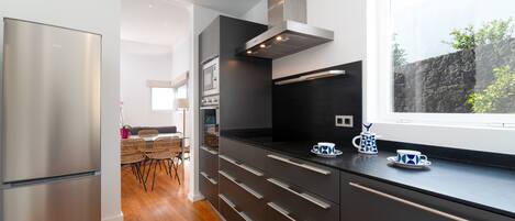 A modern kitchen with stainless steel appliances, a black countertop, and a window overlooking a stone wall.