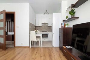 Cocina compacta con armarios blancos, una mesa de comedor y un televisor.