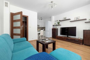 Una sala de estar con sofá, mesa de centro, televisor y cocina al fondo.