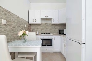 A compact kitchen with white cabinets, a stove, oven, microwave, and a dining table with a vase of flowers. - Turquoise Apartment | Large Terrace (Kraków)