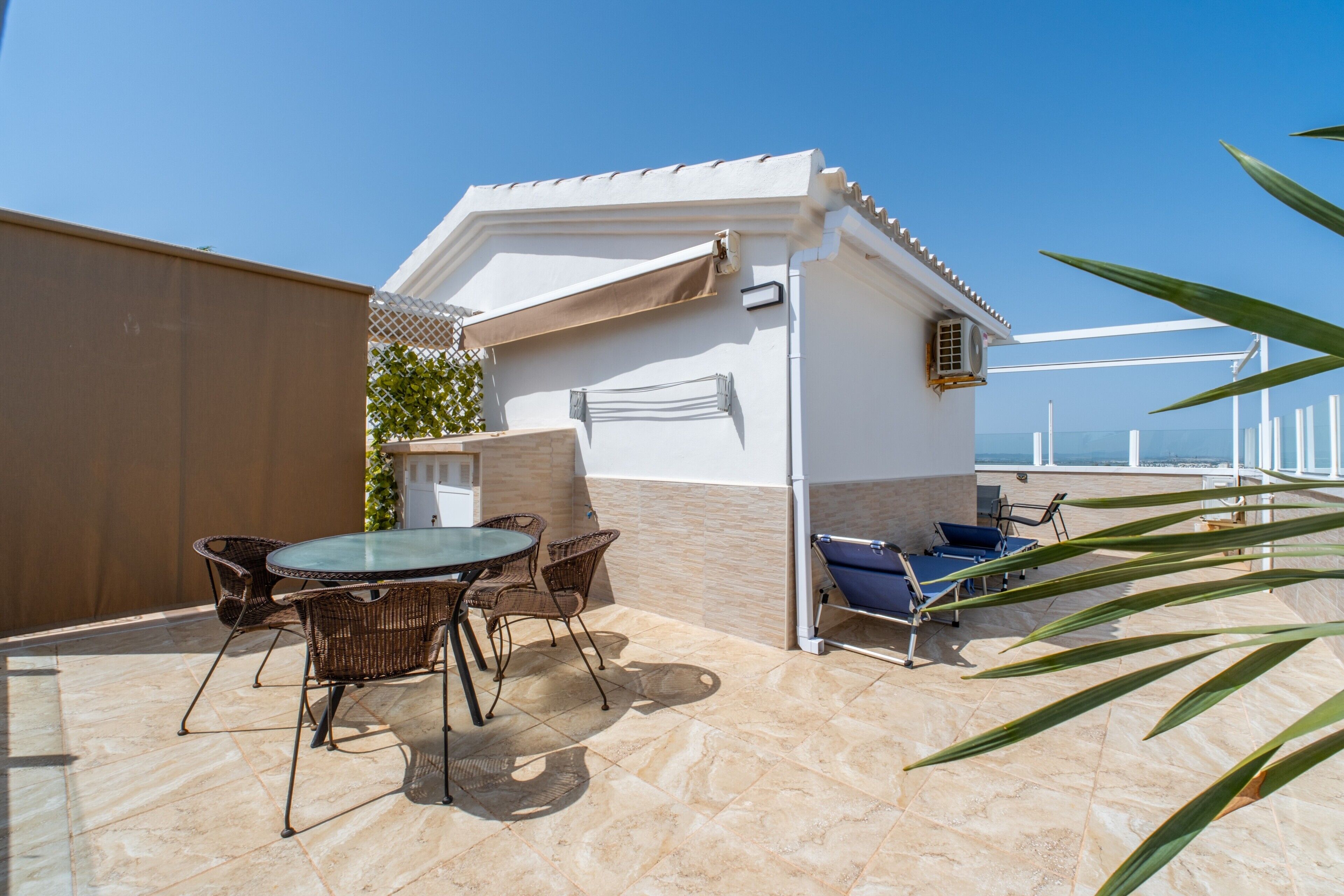 Une terrasse avec une table et des chaises, un petit bâtiment où est accrochée une serviette, et une vue sur la mer.