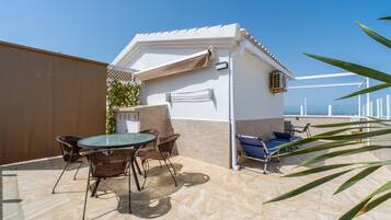 A patio with a table and chairs, a small building with a towel hanging, and a view of the sea.