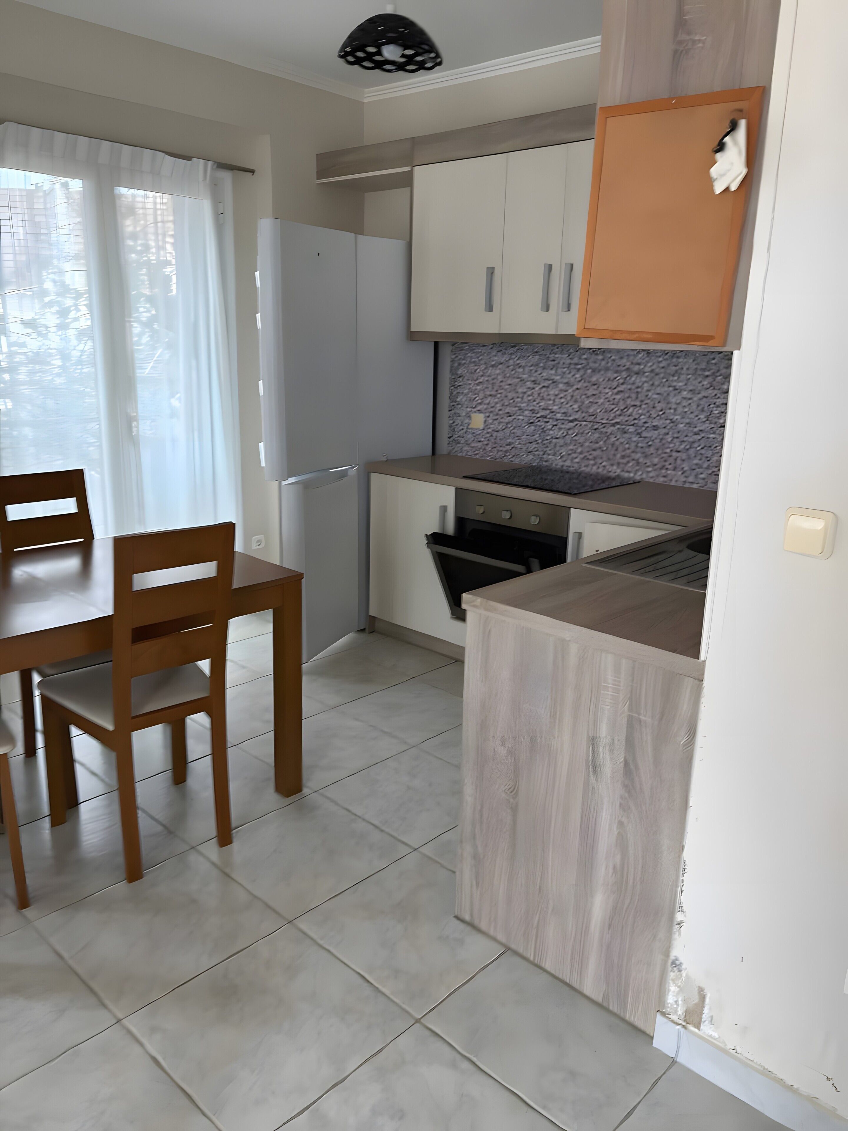Een kleine keuken met een eethoek, met kastjes, een aanrecht en een eettafel met stoelen.
