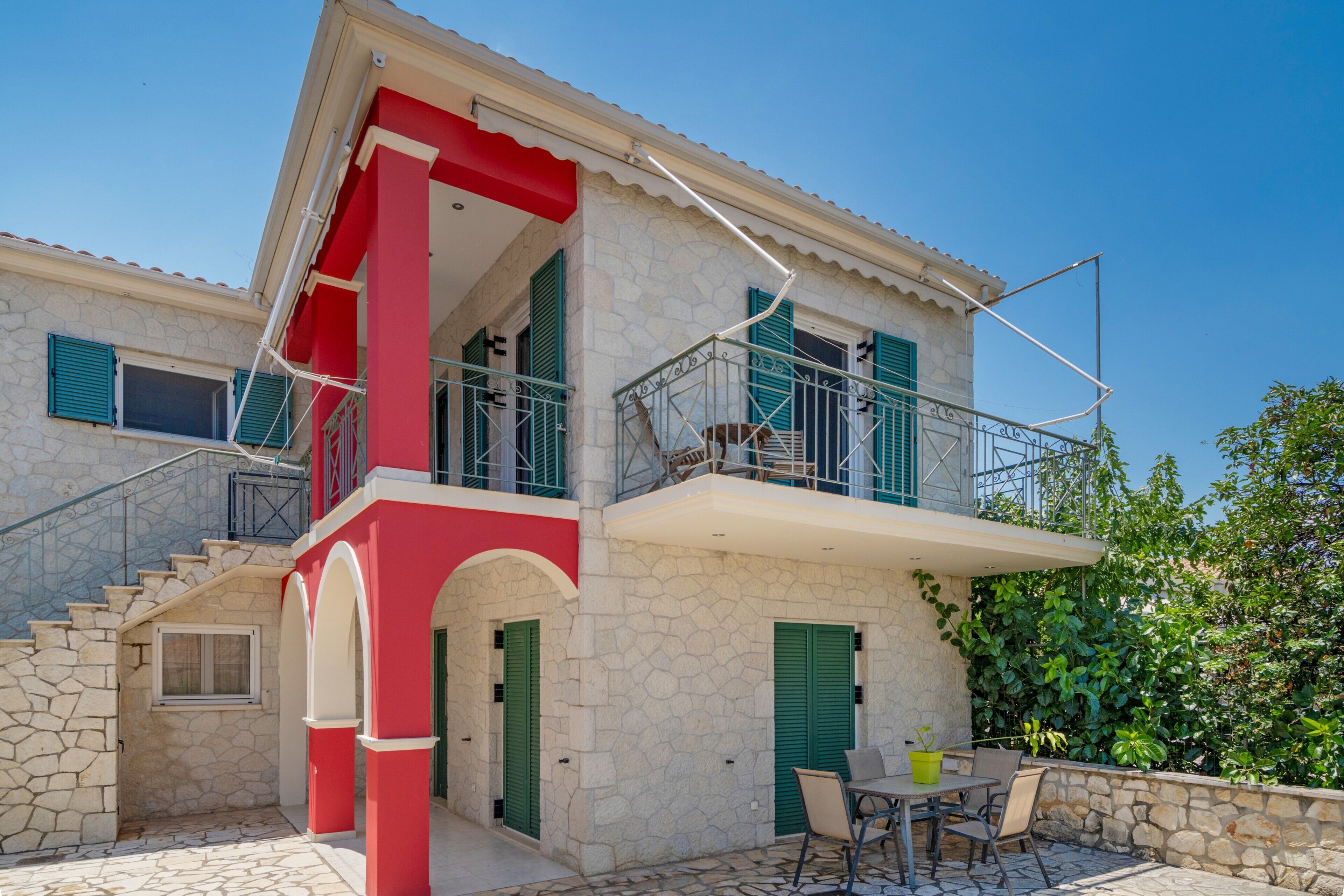 Una casa de piedra de dos pisos con balcón, escaleras y un patio con muebles de exterior.