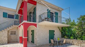 Una casa de piedra de dos pisos con balcón, escaleras y un patio con muebles de exterior.