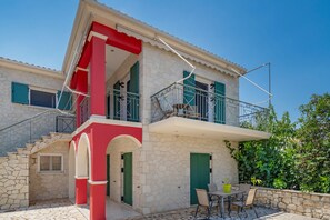 A two-story stone house with a balcony, a staircase, and a patio area with outdoor furniture.