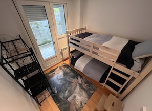Een kamer met een stapelbed, een radiator, een raam met zonwering en een zwart metalen rek.