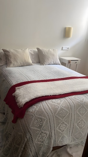 Un llit ben fet amb un estovat estampat i una manta vermella i blanca.