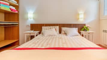 Una cama bien hecha con ropa de cama floral, una mesita de noche con una lámpara y un estante con toallas dobladas.