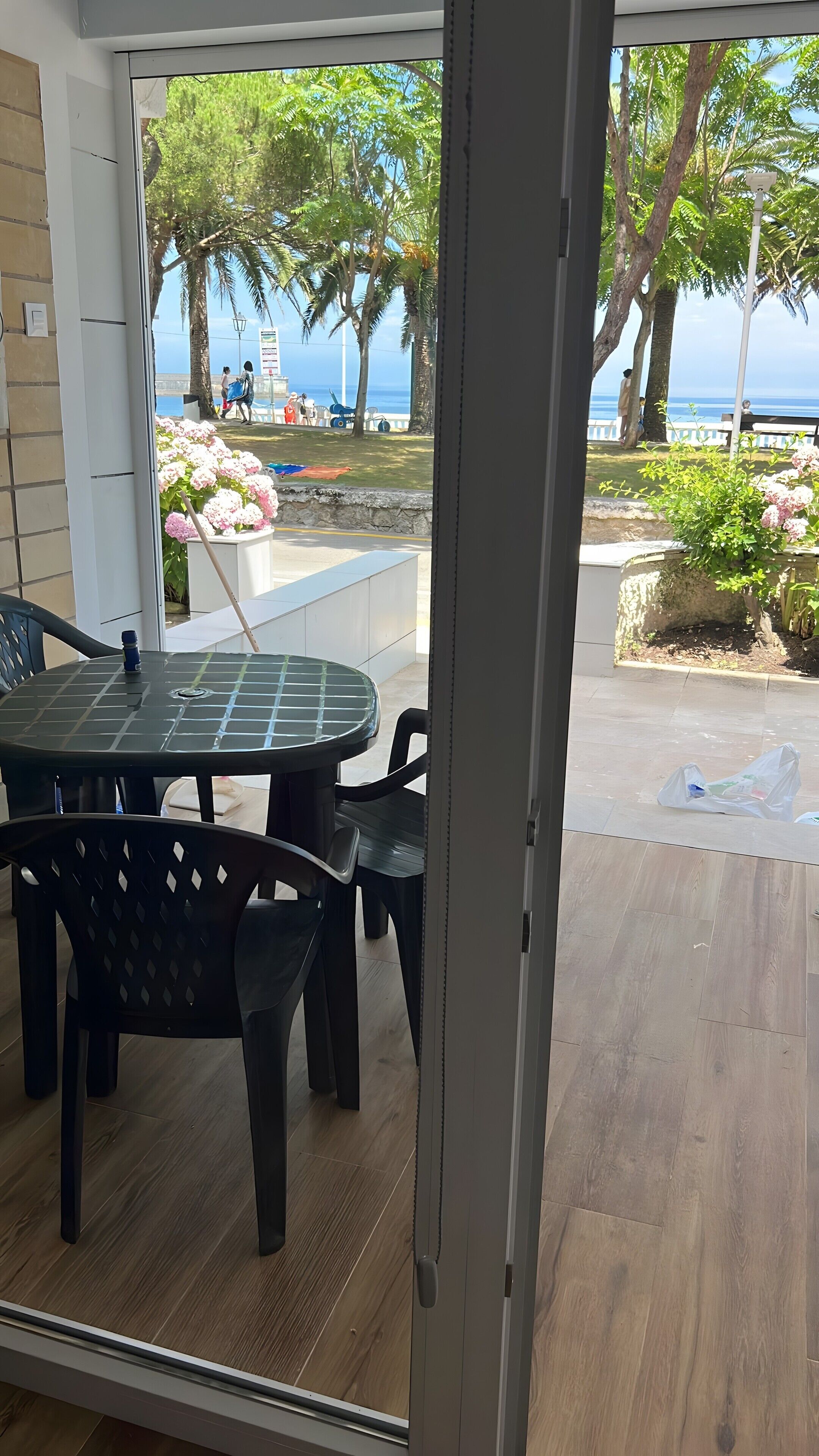 Een kamer met een glazen deur die uitkomt op een balkon met uitzicht op het strand en palmbomen.