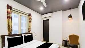 A bedroom with a bed, a ceiling fan, an air conditioning unit, a desk with a chair, and a hanging light fixture. - Super Deluxe Room Townhouse Alwal Rd (Hyderabad)