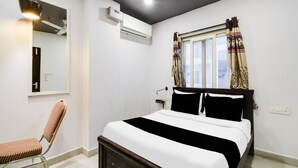 A bedroom with a bed, a chair, a ceiling fan, an air conditioning unit, and a window with curtains. - Super Deluxe Room Townhouse Alwal Rd (Hyderabad)