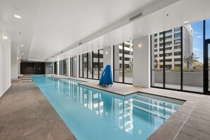 A modern indoor swimming pool with a long, narrow design, large windows, and a covered area with a blue canopy. - Luxurious 2BR In Sought-After `Eastbourne` Complex (Parkes)