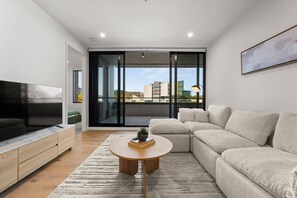 Un salon moderne doté d’un téléviseur à écran plat, d’un canapé beige, d’une table basse et d’un balcon offrant une vue sur la ville.