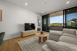 Ein modernes Wohnzimmer mit Flachbildfernseher, einer Couch, einem Couchtisch und Blick auf die Stadt durch große Fenster.