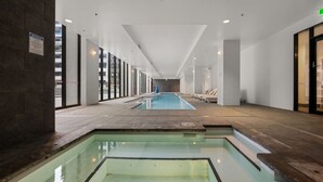 En lång inomhuspool med väggar av genomskinligt glas, ett kaklat golv och en skylt som anger reglerna för spa-området.