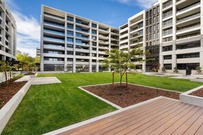 A modern multi-story building with a central courtyard featuring grass, trees, and a wooden deck. - Luxurious 2BR In Sought-After `Eastbourne` Complex (Parkes)