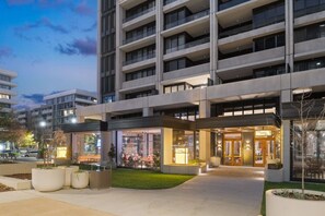 Ein mehrstöckiges Hotel mit zentralem Eingang, Außenbereich mit Sitzgelegenheiten und einer gut beleuchteten Fassade.