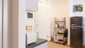 Ett kök med ett svart kylskåp, en hylla med köksredskap, en brandsläckare och ett konstverk som hänger på väggen.