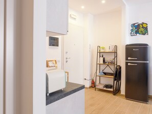 A kitchen with a black refrigerator, a shelf with kitchen items, a fire extinguisher, and a wall-mounted artwork. - At Francesca's House - Balduina 88 (Roma)