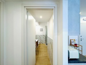 Un pasillo con piso de madera que conduce a un baño con pared de mármol y lavamanos.