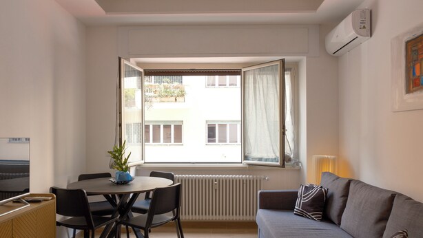 Ett rum med ett matbord, stolar, en soffa, ett element och ett fönster med gardiner.