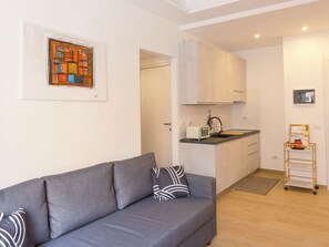 A modern living room with a grey sofa, a small kitchen area with a toaster and kettle, and a wooden side table. - At Francesca's House - Balduina 88 (Roma)