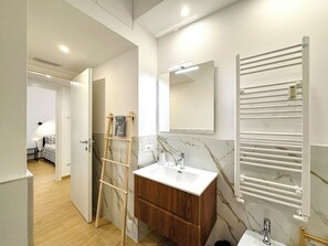 Un baño moderno con tocador de mármol, una escalera de madera, un perchero y un espejo.