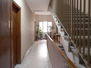 A hallway with a wooden door, potted plants, a staircase with a wooden railing, and a window providing natural light. - At Francesca's House - Balduina 88 (Roma)