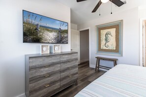 Ein Schlafzimmer mit Bett, Kommode, einem Gemälde mit Strandmotiv und einem Gemälde eines Seepferdes sowie einem Deckenventilator.