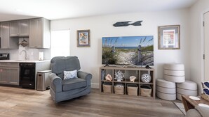 Un salon moderne avec un canapé gris, un tableau représentant une plage et un meuble en bois agrémenté d’objets décoratifs.