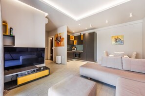 Ein modernes Wohnzimmer mit Flachbildfernseher, einer Couch, einem Essbereich mit Tisch und Stühlen sowie einer Küche mit Schränken und Geräten.