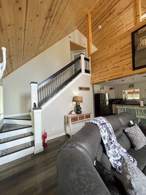 A modern interior with a staircase, a living area with a sofa, and a kitchen in the background.