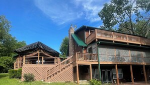 Une cabane en rondins à deux étages, dotée d’une cheminée en pierre, d’un balcon et d’une terrasse couverte.