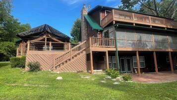 Une cabane en rondins à deux étages, dotée d’une cheminée en pierre, d’un balcon et d’une terrasse couverte.