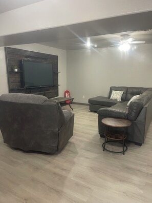 A living room with a flat-screen TV, two grey sofas, a small round table, and a ceiling fan. - Large Spacious home with Awesome Lake Access with dock and boat slip (Shell Knob)