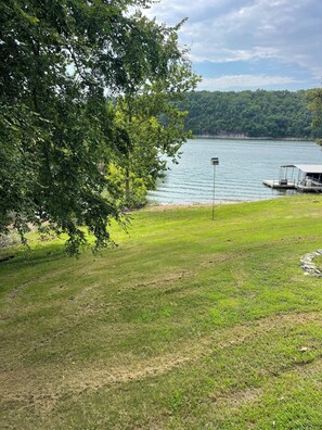 A grassy area with a dock and a boat, a lake, and a forested hill in the background.