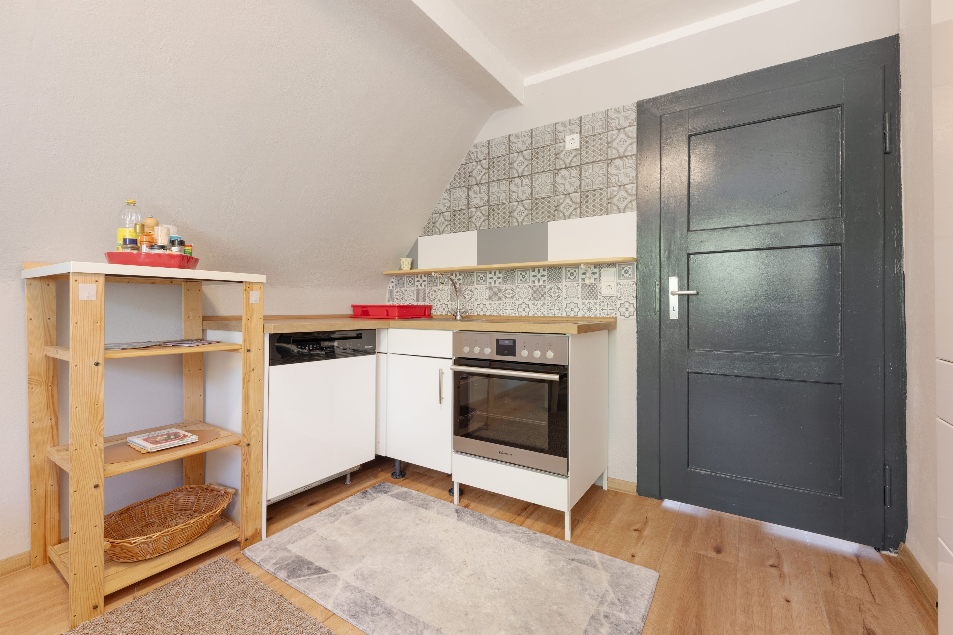 A compact kitchen with white cabinets, a dishwasher, an oven, and a black door.