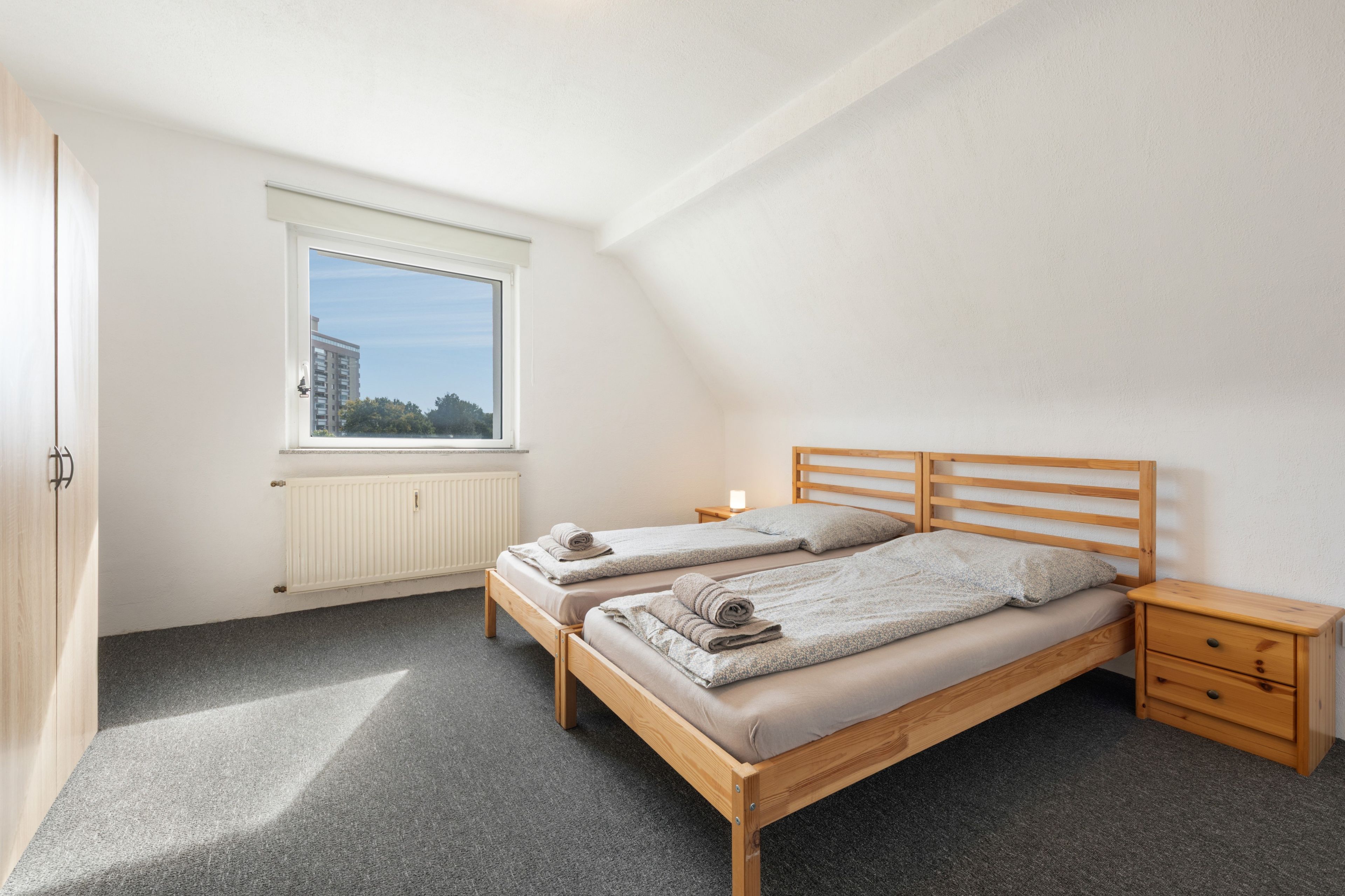 A bedroom with two single beds, a window, a radiator, and a small bedside table with a lamp.