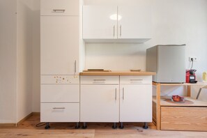 A compact kitchen with a white cabinet, a wooden countertop, and a built-in refrigerator.