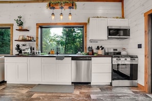 A modern kitchen with white cabinetry, a built-in oven, a microwave, and a large window.