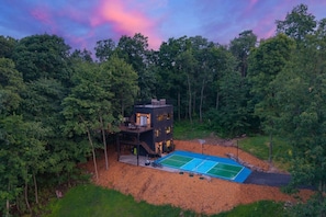 A modern house surrounded by trees with a tennis court.