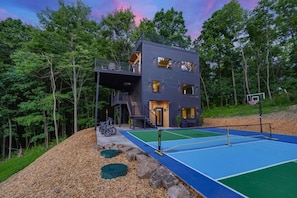 A multi-story building with a balcony, a basketball court, and a surrounding wooded area.