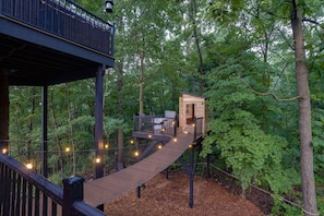 A wooden treehouse with a rope bridge, surrounded by dense forest.