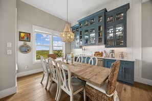 Un comedor con una mesa y sillas de madera, una araña y una cocina con armarios azules.